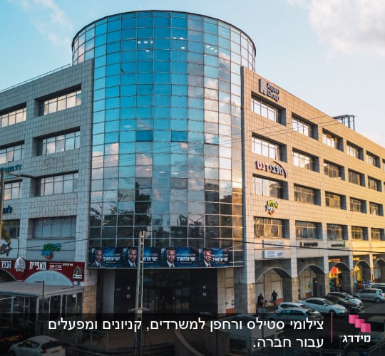 בניין עם חזית זכוכית, מכוניות חונות, שמיים מעוננים